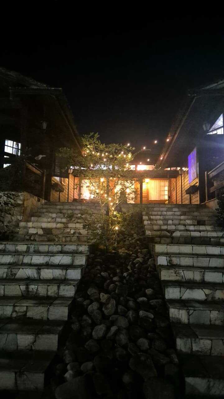 Entrada noturna da casa-mãe com escadaria iluminada entre as árvores