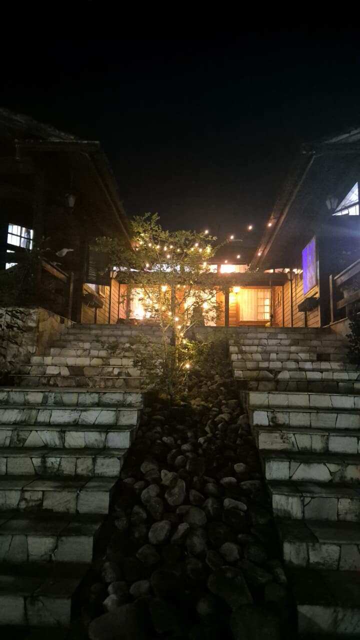 Entrada noturna da casa-mãe com escadaria iluminada entre as árvores