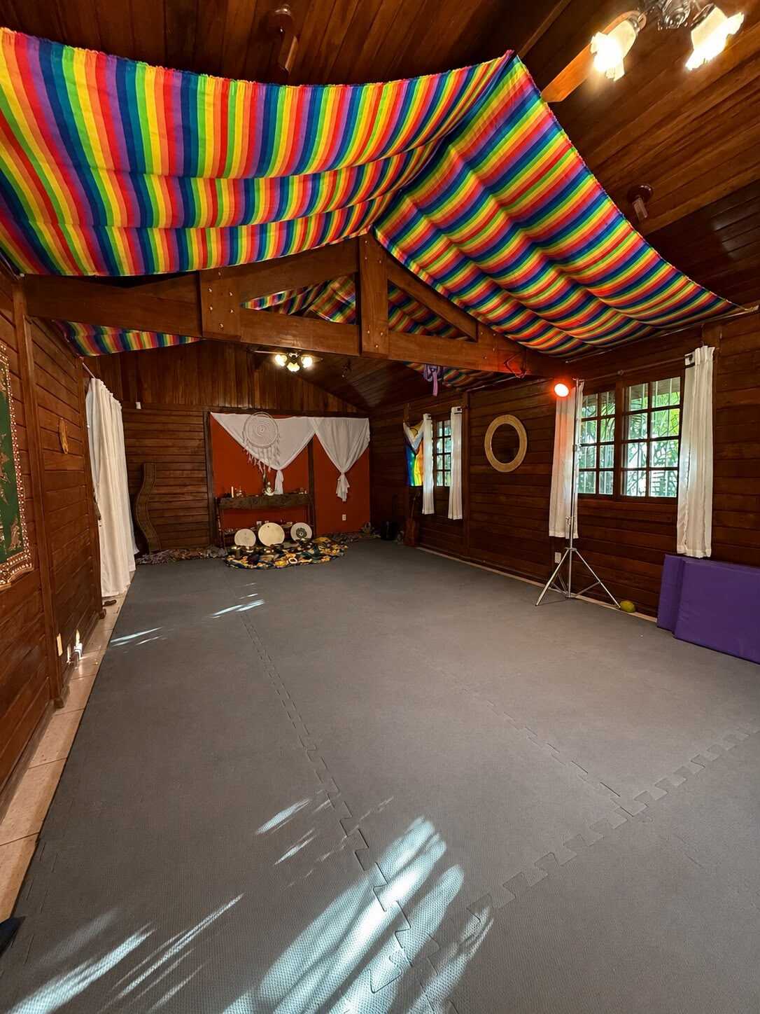 Sala de vivências da casa-mãe com teto de tenda em arco-íris, tatames e altar ao fundo