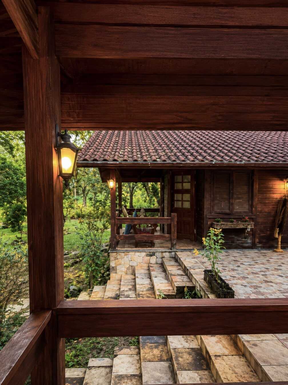 Varanda de madeira da casa-mãe com lampião aceso e piso de tijolo, ao entardecer